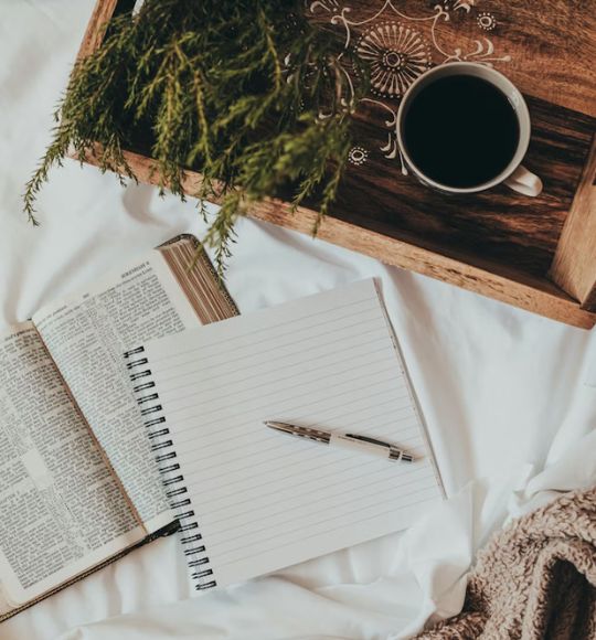 A cozy scene featuring a notebook, a pen, and a steaming cup of coffee resting on a bed, image for Beacon Psychiatry in Trinity, Florida